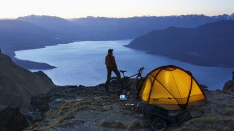 Man standing on hilltop with tent and Rambo e-bike while enjoying the view